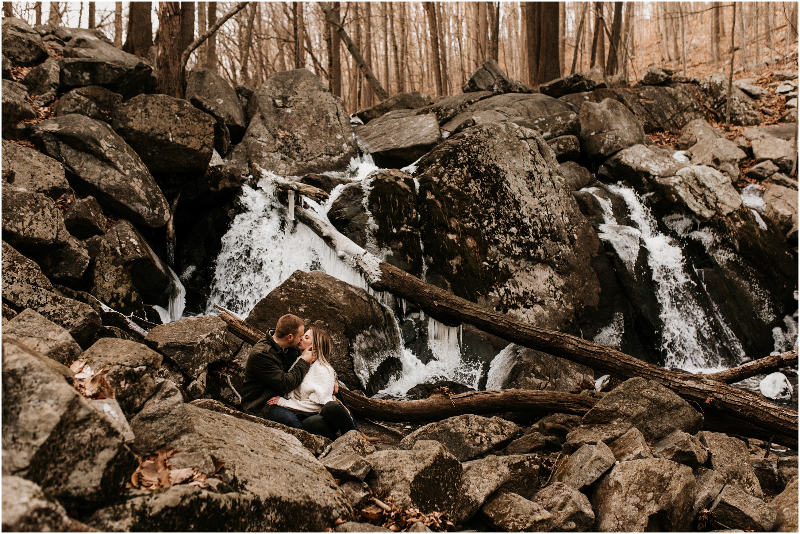 Couple hiking engagement session kissing in the woods by a waterfall