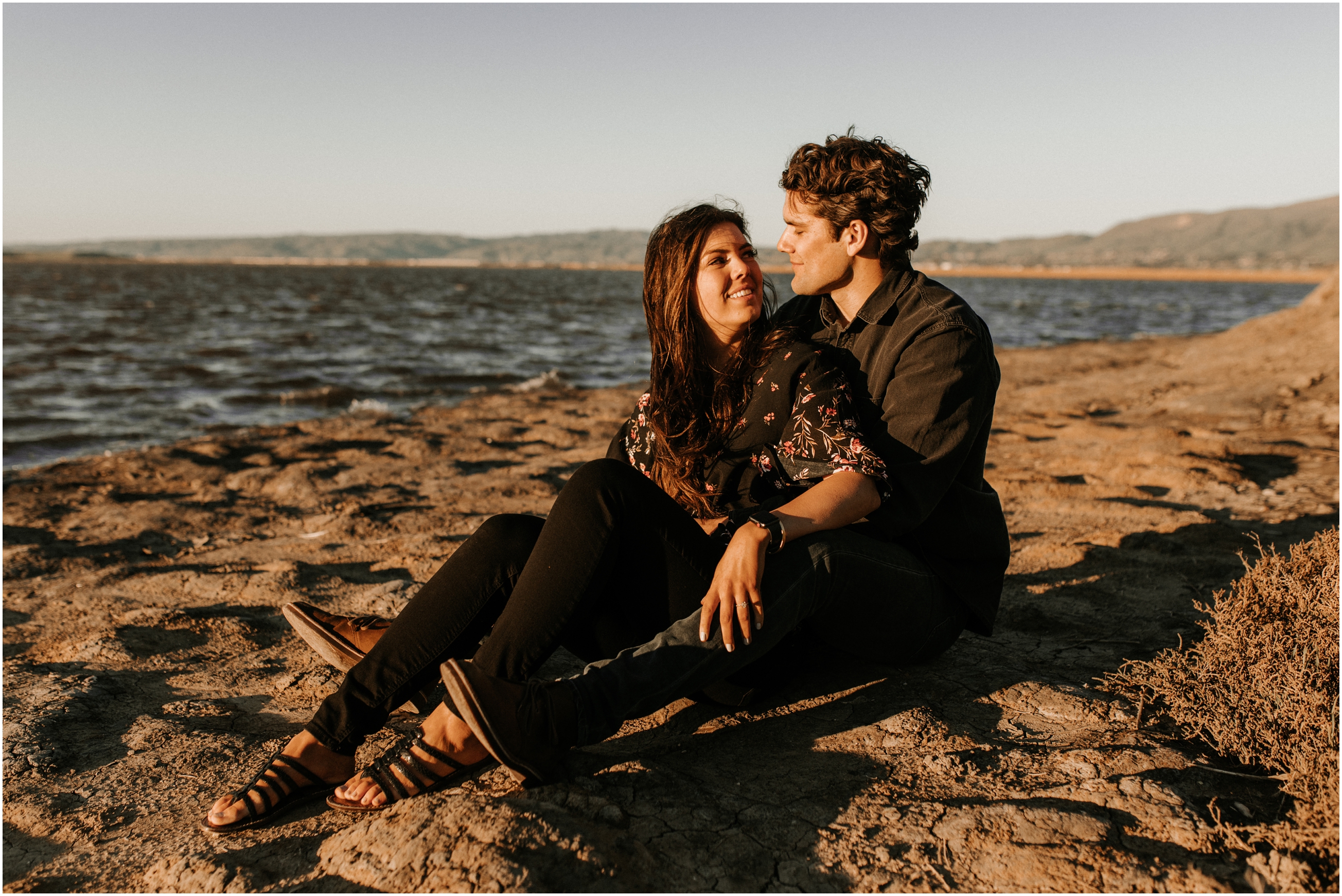 couple sitting in sand at sunset on windy beach in bay area california