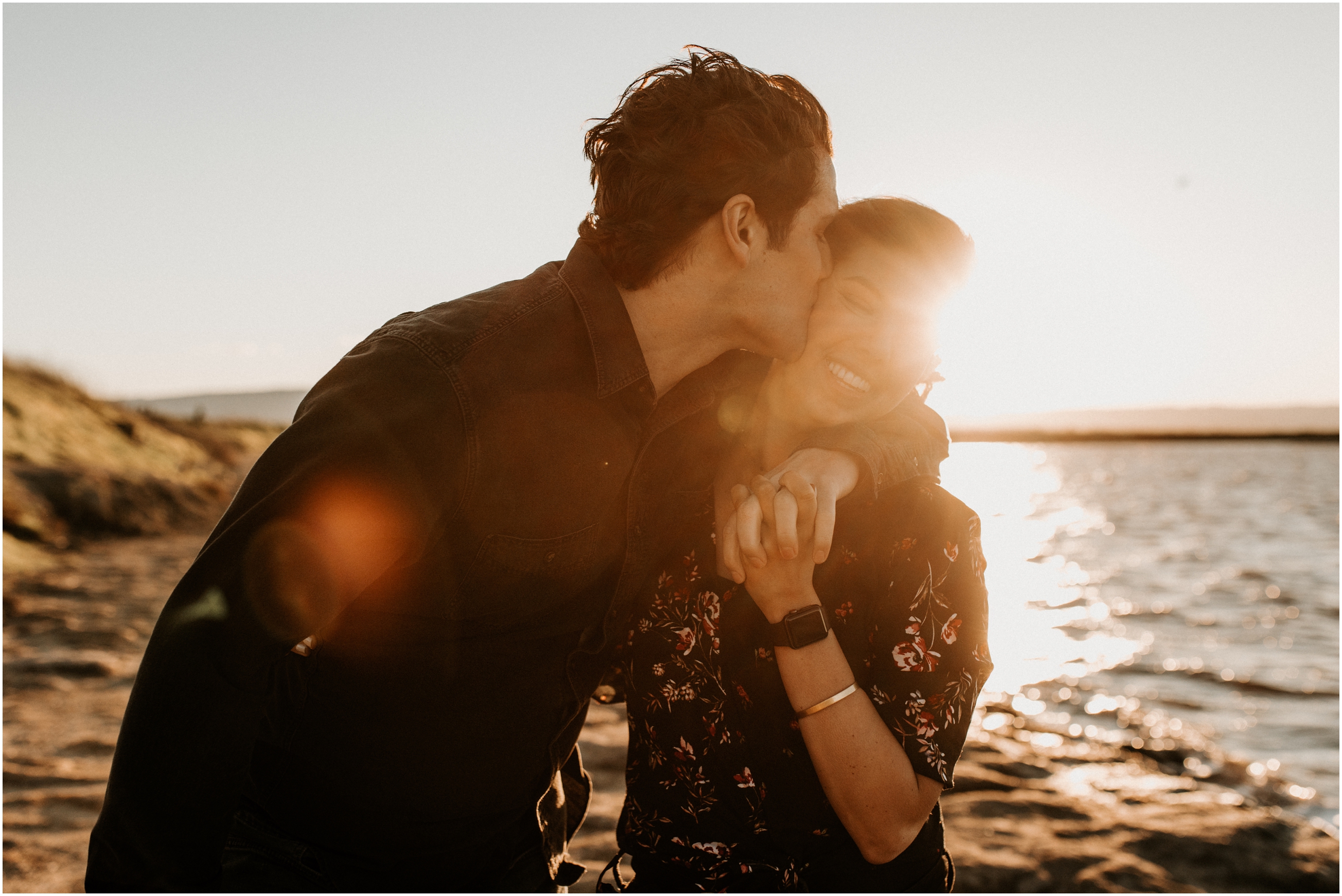 husband kissing wife's cheek at sunset on windy beach in bay area california