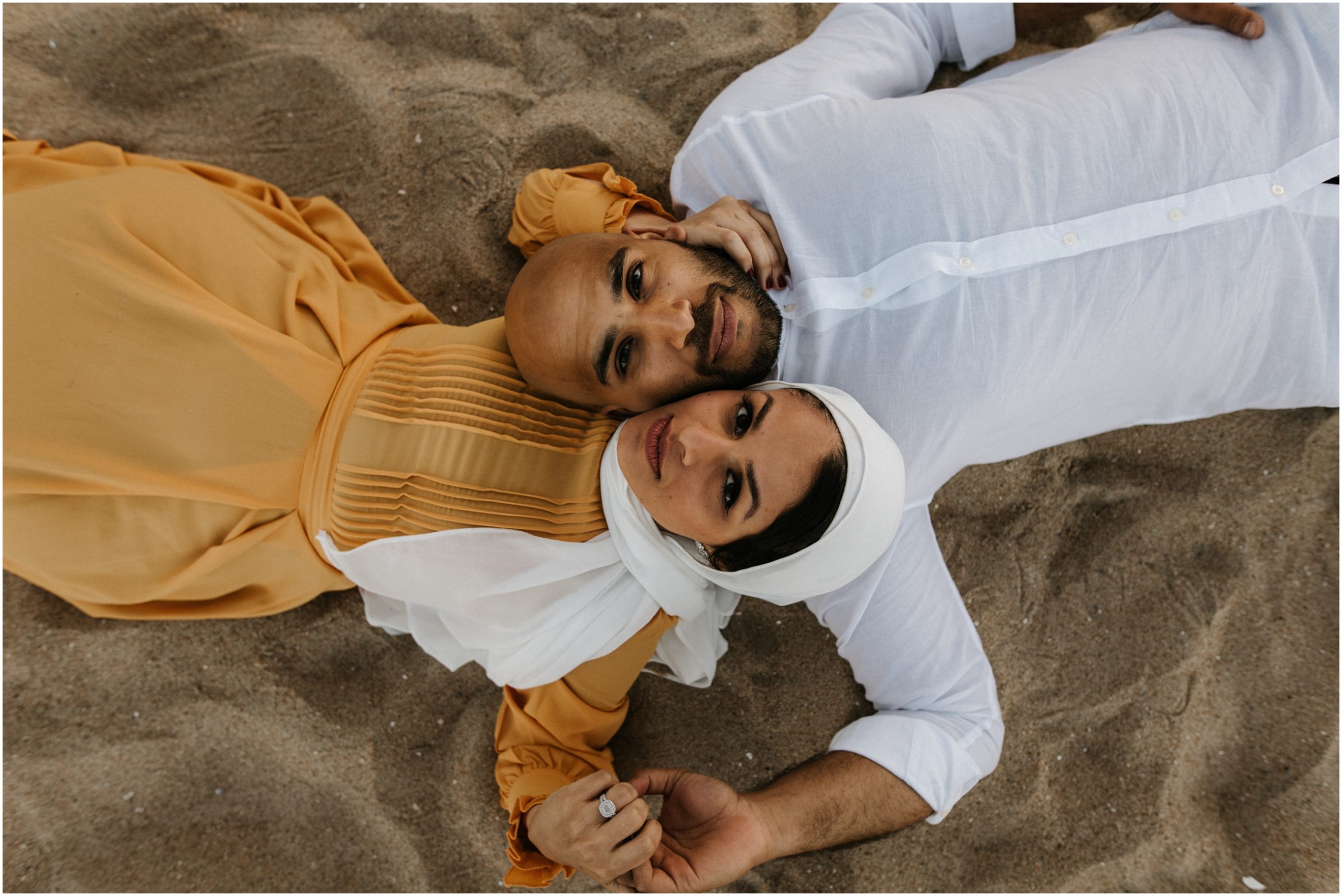 couple lying on sand looking up at camera