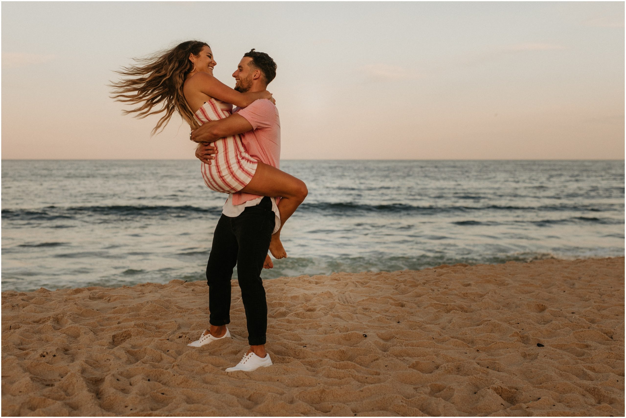 man lifting woman up and laughing on beach in long branch new jersey