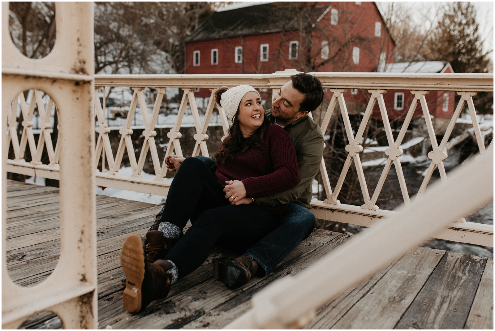 couple sitting on bridge in snow at red mill museum in clinton, nj