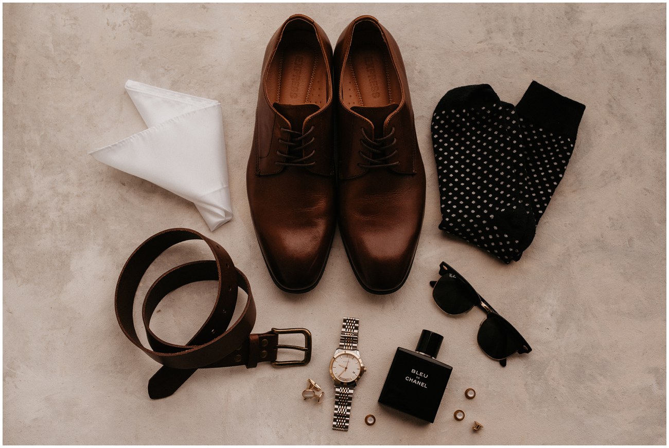 flat lay of groom wedding details including shoes, belt, watch, glasses, cologne, pocket square and socks