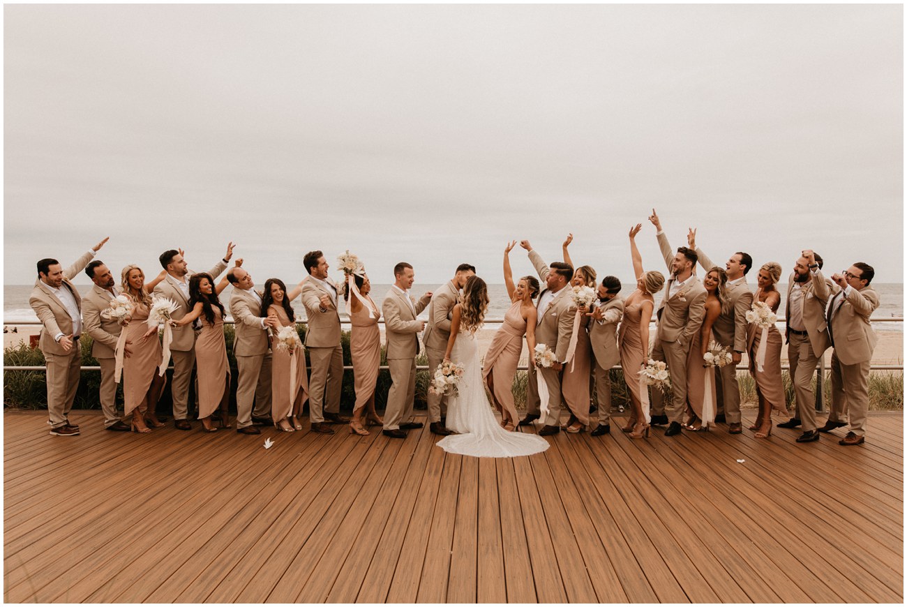wedding party cheering while bride and groom kiss on boardwalk at Wave Resort in Long Branch, NJ