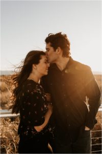 husband kissing wife's forehead at sunset on windy beach