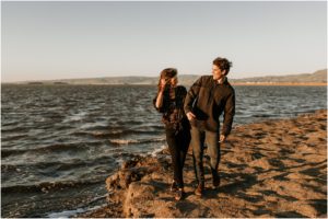 couple walking along water's edge at sunset on windy beach in bay area california