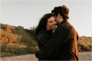 couple hugging at sunset on windy beach in bay area california