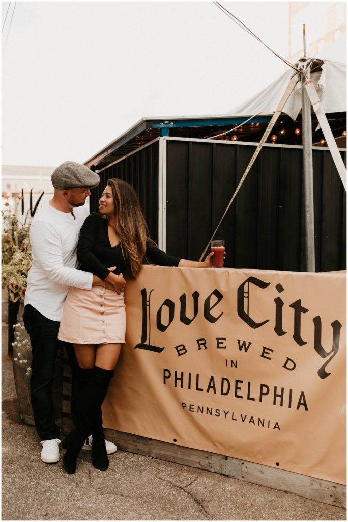 Couple shares a beer in front of Love City Brewed sign in Philadelphia