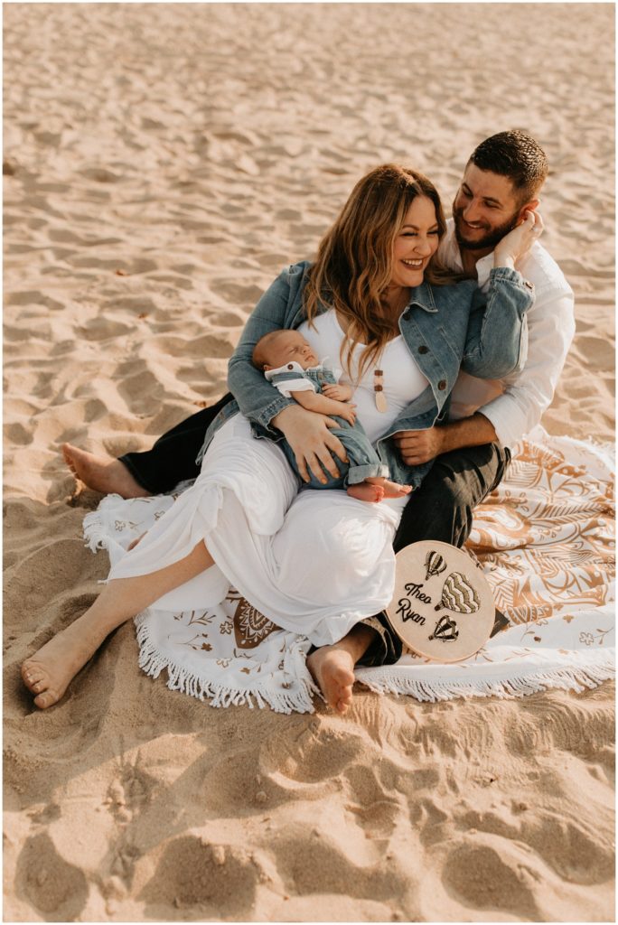 Parents and newborn baby cuddle on the Ocean Grove beach