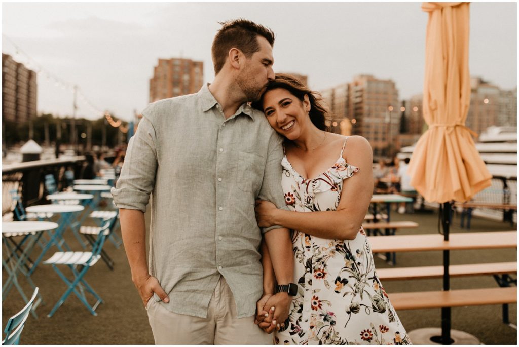 couple poses together in front of tables and chairs at Pier 13 in Hoboken