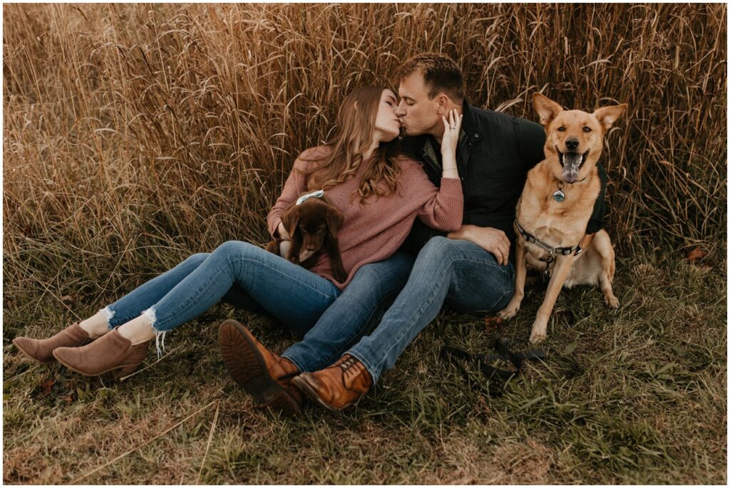 Couple kisses with two dogs in a field  for fall Historic Smithville Park mini sessions